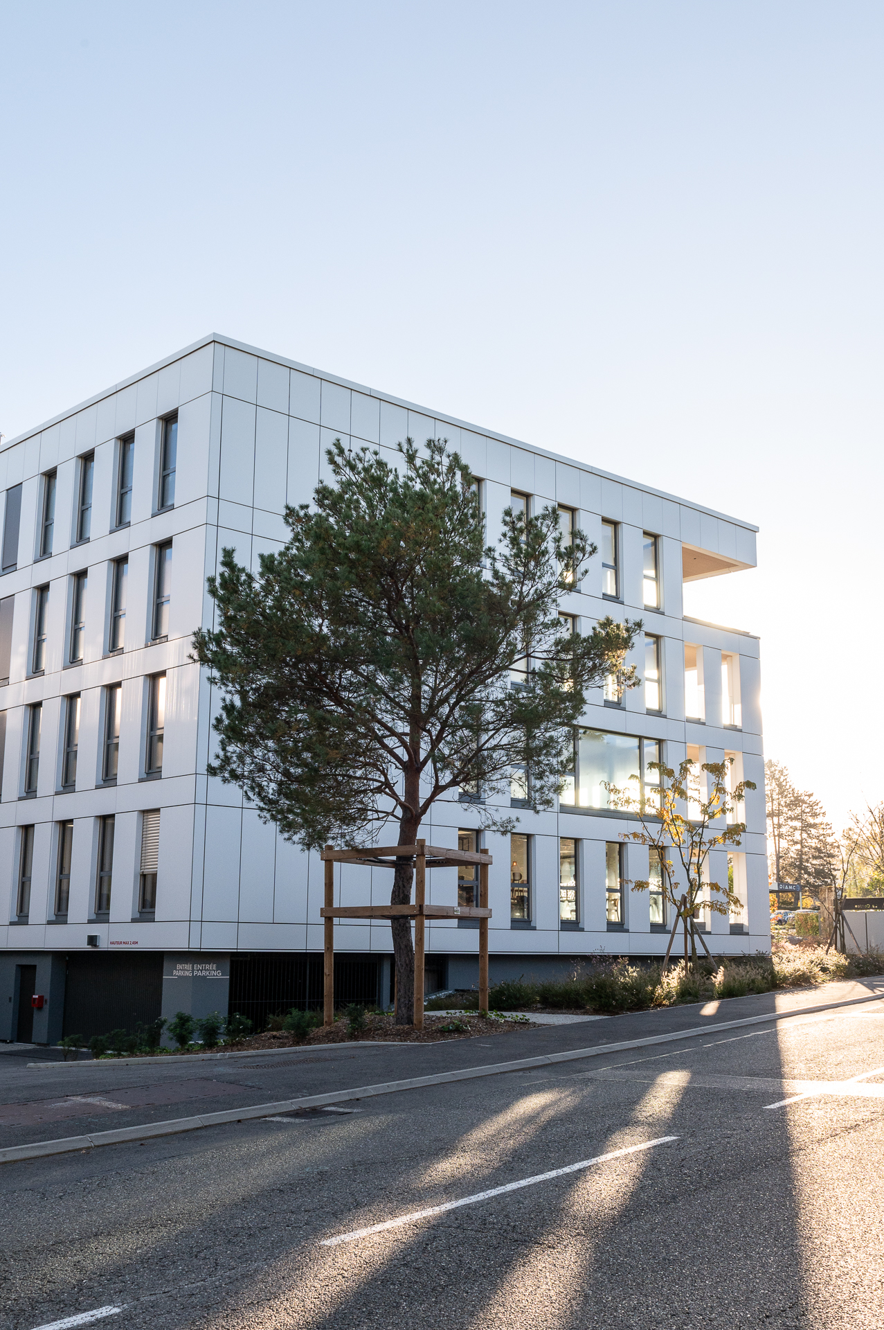 Façade d'un bâtiment de bureaux moderne à l'architecture blanche géométrique, vue en contre-plongée depuis la rue, réalisé pour la foncière du Crédit Agricole des Savoie.