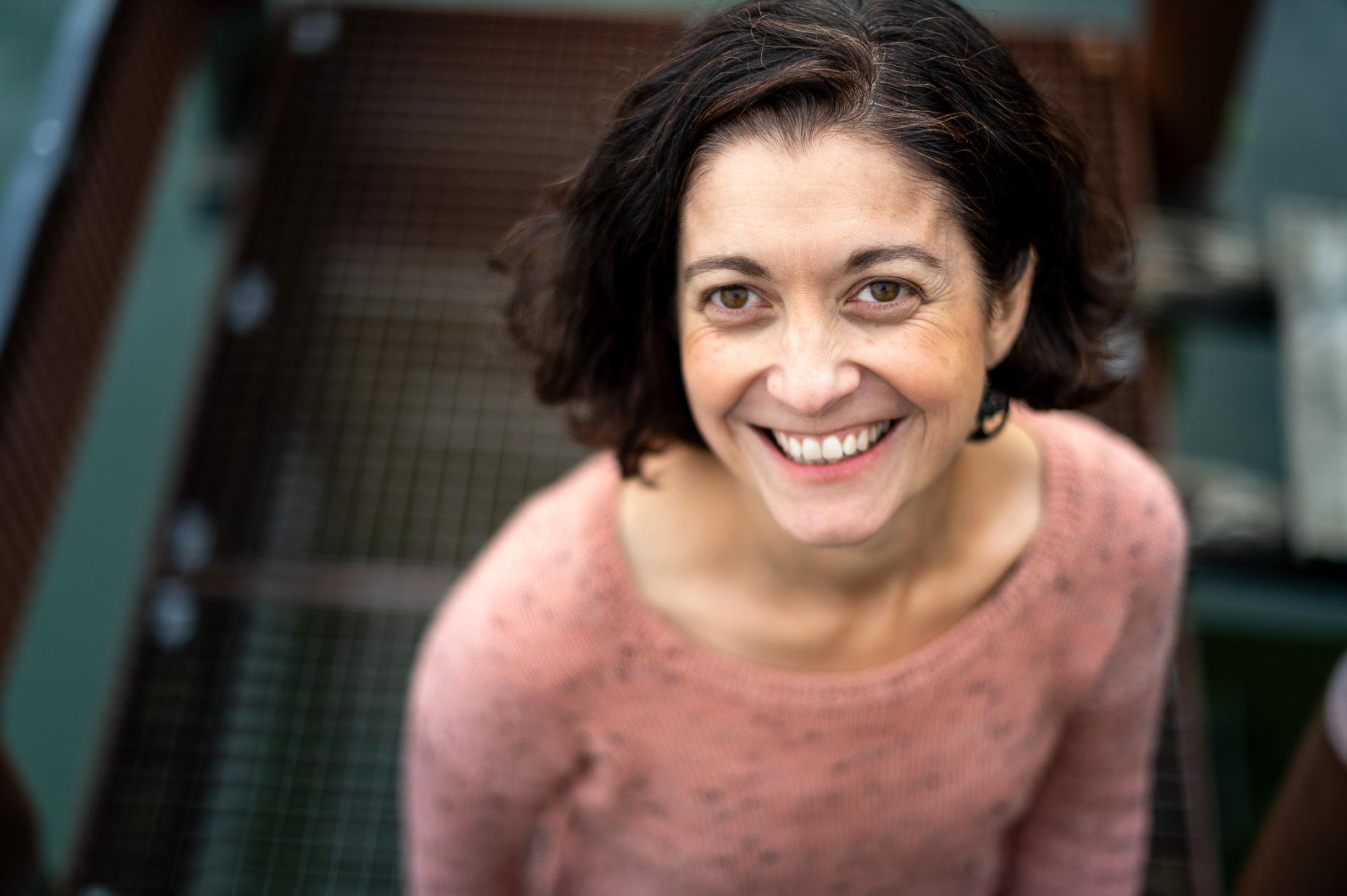 Portrait souriant de Céline Messina, fondatrice de Mlle Pétronille, pull rose, pris en légère plongée sur un escalier métallique.