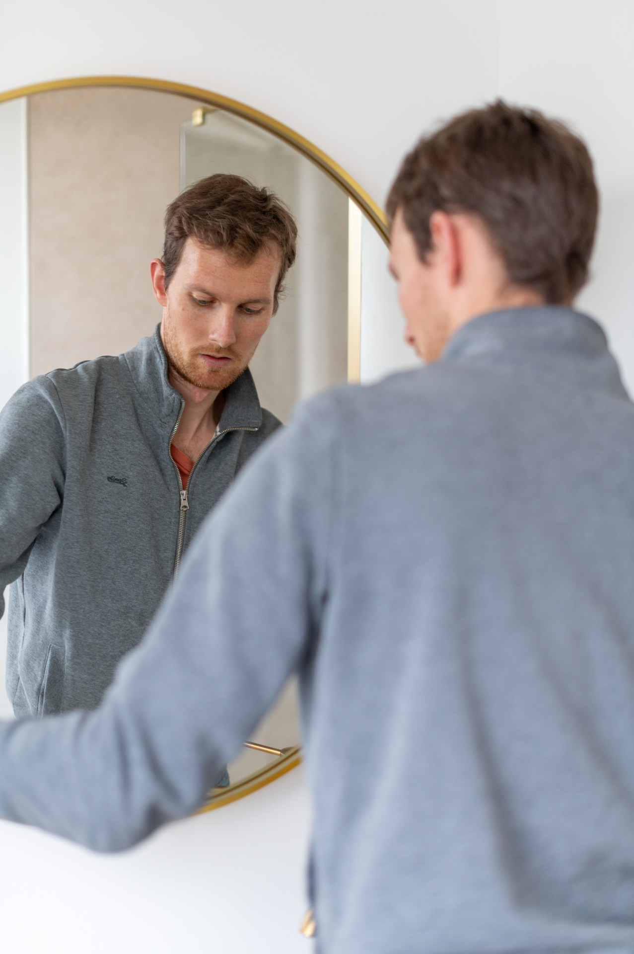Un homme ajuste sa tenue devant un miroir rond doré, avec un jeu de reflet, portrait pour l'entreprise TP Elec.